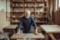 Senior potter standing and leaning on table against shelves with pottery goods at workshop Royalty Free Stock Photo