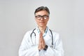 Senior professional male doctor or physician in white coat with stethoscope around neck praying, looking at camera while Royalty Free Stock Photo