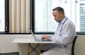 Senior professor with mustache and beard typing on laptop computer keyboard. Sitting near the window in cafeteria. Outside the Royalty Free Stock Photo