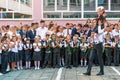 Senior pupil carries first-former girl ringing with golden bell against schoolchildren. Tradition of beginning of elementary