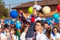 Senior pupil carries first-former girl ringing with golden bell against schoolchildren. Tradition of beginning of elementary