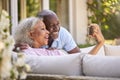 Senior Retired Couple Sitting Outside In Garden At Home Making Video Call On Mobile Phone Royalty Free Stock Photo