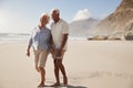 Senior Retired Couple Walking Along Beach Hand In Hand Together