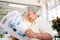 A senior retired man in casual clothes is concerned with reading a newspaper about COVID-19 news. While sitting at home. Royalty Free Stock Photo