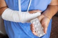 A senior retired woman with a rewound arm in a cast and a bandage holds anesthetic pills. Blow, fracture, bones, hospital