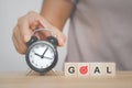 hand holding black analog alarm clock and goal text on wooden cube for target , aiming concept Royalty Free Stock Photo