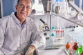 Senior scientist man wearing white dress coat sitting in laboratory at work place