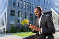 Senior smiling African American man businessman in suit sitting on bench outside office center wearing headphones and Royalty Free Stock Photo