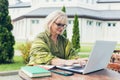 Senior beautiful business woman sitting on a chair and making notes in a notebook, with a phone and laptop in the yard Royalty Free Stock Photo