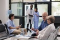 Senior specialist sitting on chair in hospital lobby explaining illness diagnosis to elderly patient