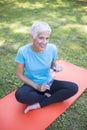 Senior sportive woman sitting on mat outside and resting after workout