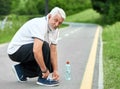 Senior sportsman tie sneakers laces sitting on race track, looking at camera.