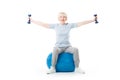 Senior sportswoman with dumbbells in wide hands sitting on fitness ball