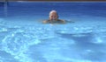 Senior sporty woman smiling while swimming in outdoor swimming pool on a sunny day - active retiree attentive to his physical well