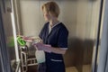 Professional chambermaid wearing uniform and gloves cleaning elevator with detergent and rag Royalty Free Stock Photo