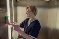 Professional chambermaid wearing uniform and gloves cleaning elevator with detergent and rag Royalty Free Stock Photo