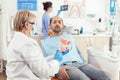 Senior stomatologist explaining to sick patient dental procedure