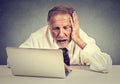 Senior stressed man working on laptop sitting at table isolated on gray wall background Royalty Free Stock Photo
