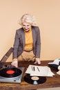 senior stylish woman turning on vinyl record player at table with typewriter