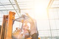 Senior supervisor instructing young female farmer driving forklift in greenhouse with yellow lens flare in background