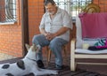 Senior talks to dog sitting near his house. The dog listen him with consideration