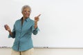 Senior teacher pointing while gesturing against white board in classroom