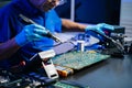 Senior technician soldering a circuit board on workbench. Blue gloves, precision tools, and electronics gear highlight Royalty Free Stock Photo
