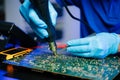 Senior technician soldering a circuit board on workbench. Blue gloves, precision tools, and electronics gear highlight real people Royalty Free Stock Photo
