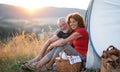 Senior tourist couple with picnic basket sitting in nature at sunset, resting.