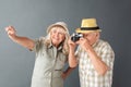 Senior tourists in beach hats studio standing isolated on gray holding camera taking photos cheerful