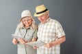 Senior tourists in beach hats studio standing on gray holding map and browsing internet on digital tablet