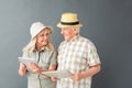 Senior tourists in beach hats studio standing isolated on gray holding map using digital tablet looking at each other