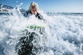 Senior trying to surf a wave on the sea at the beach alone with black wetsuit and green surftable - vacation at the sea and active