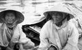 Senior Vietnamese couple sitting their small boat in river sheltering from rain in conical hats and plastic covers