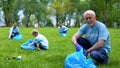 Senior volunteer with plastic bag picking up litter in forest, responsibility