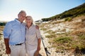 Senior white couple standing on a beach embracing and smiling to camera, three quarter length