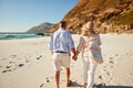 Senior white couple walking on a beach holding hands, back view, three quarter length, close up