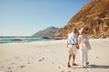 Senior white couple walking on a beach together holding hands, full length, back view