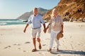 Senior white couple walking on a beach together holding hands, full length, close up