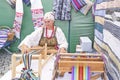 Senior white woman at pavilion of traditional Irbit fair weaving colorful striped belt on hand loom Royalty Free Stock Photo