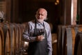 Senior winemaker tasting red wine near a big oak barrel