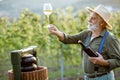 Senior winemaker with wineglass and press machine on the vineyard