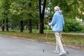 Senior woman active lifestyle. Caucasian aged lady in blue hoodie does nordic walking in the park outdoor in late summer Royalty Free Stock Photo