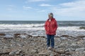 Senior woman alone, walking along on rocky beach Royalty Free Stock Photo