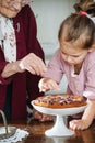 Senior woman along with her granddaughter pouring powdered sugar on tasty pie