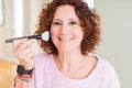 Senior woman applying blush on face using a brush with a happy face standing and smiling with a confident smile showing teeth Royalty Free Stock Photo