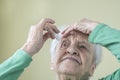 A senior woman applying eyedrops into her eyes by herself