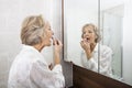 Senior woman applying lipstick while looking at mirror in bathroom Royalty Free Stock Photo