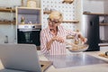 Senior woman in apron and with eyeglasses standing in kitchen, using laptop and preparing healthy meal Royalty Free Stock Photo