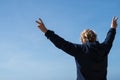 Senior woman with back facing camera holds her arms out making the peace sign against a blue sky. Concept for freedom, retirement Royalty Free Stock Photo